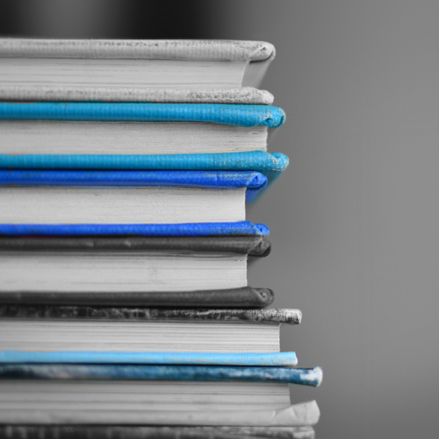 A black n white image of a pile of books. In this pile a few books with a blue cover