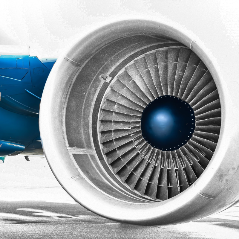A black n white image of a plane wing with the jet engine with parts of it blue.